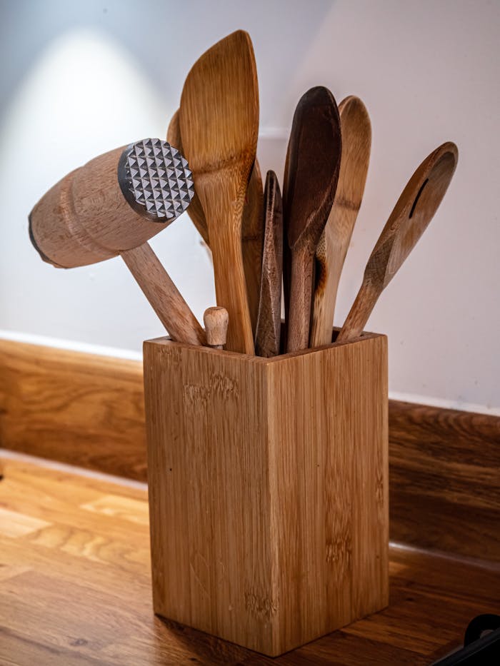 Wooden kitchen utensils and mallet in a rustic holder on a wooden surface.